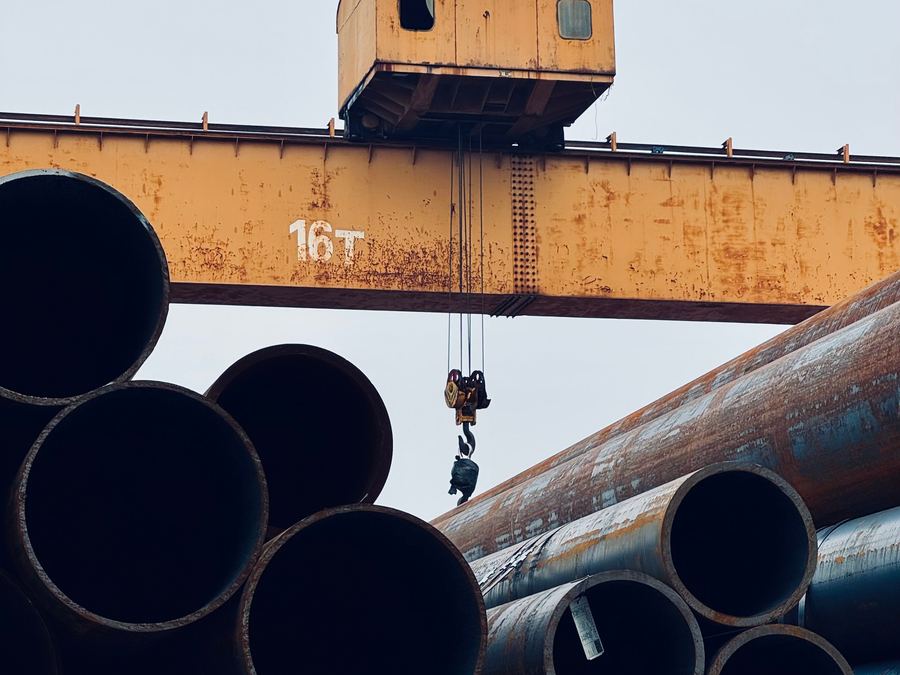 Large-diameter steel line pipe stacked beneath a gantry crane