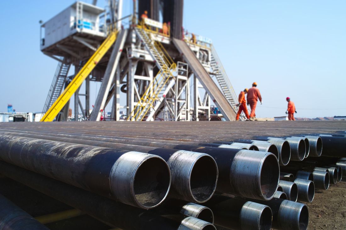 Workers beside stacked threaded tubulars at a rig site