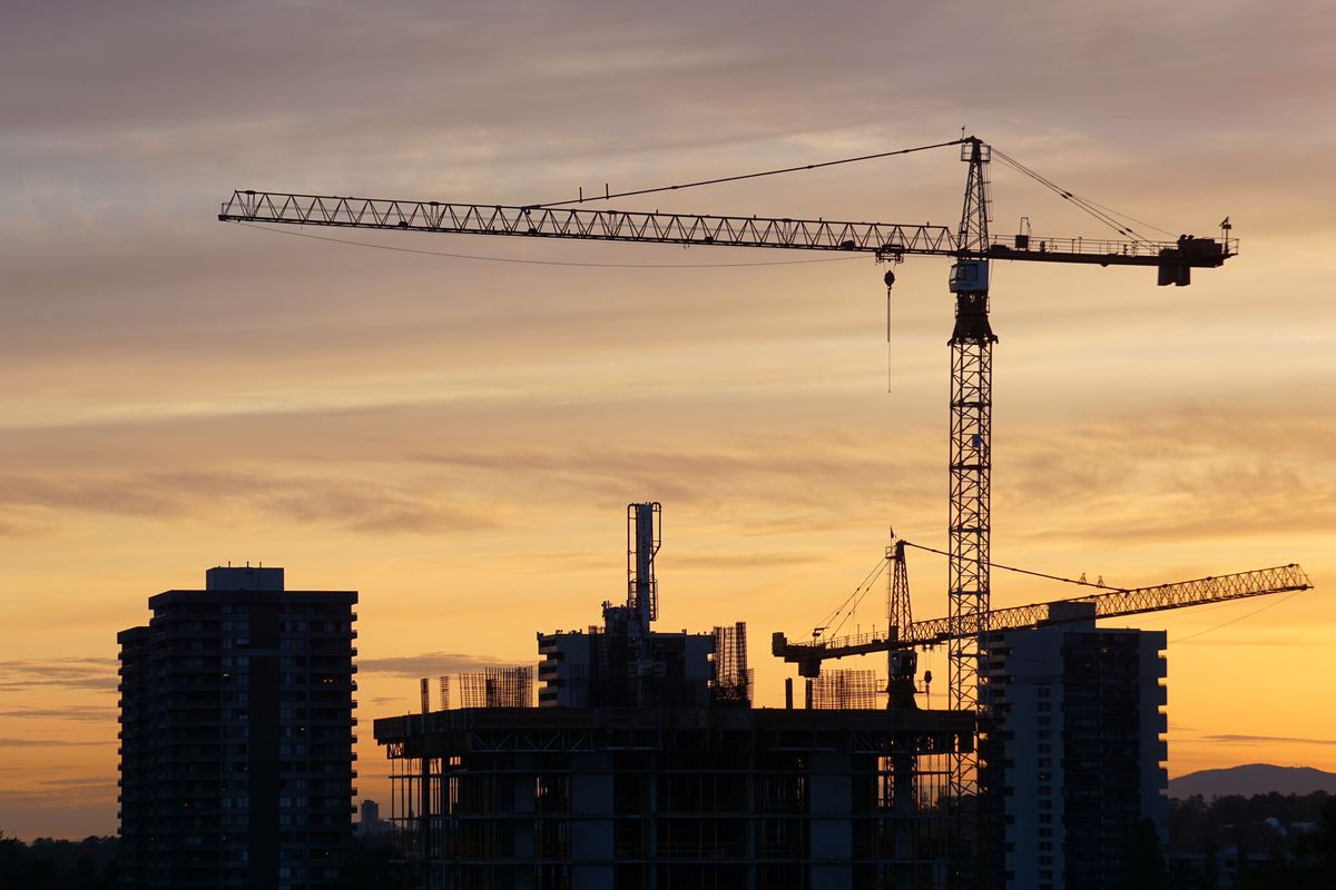 Tower cranes silhouetted against a sunset at a construction site